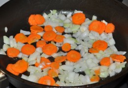Огонь под сковородой поменять на средне-сильный, засыпать нашинкованный лук и морковку, обжаривать 3,5-4 минуты, помешивая.